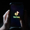 Children's hands hold a phone with the TikTok logo displayed.