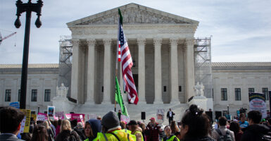 A crowd with flags and signs stand at the US Supreme Court Building.