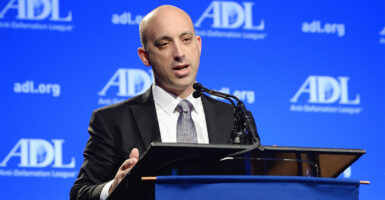 ADL CEO Jonathon Greenblatt in a suit at a podium in front of a blue wall with the ADL logo on it