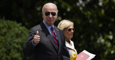 President Joe Biden in a suit with First Lady Joe Biden walking on the White House lawn. The president is giving a thumbs up.