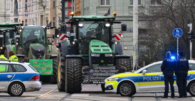 Farm tractors drive on a city street and are stopped by police cars