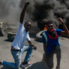 Two protesters raise their fists in the air while tires burn in the street during a demonstration