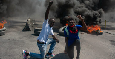 Two protesters raise their fists in the air while tires burn in the street during a demonstration
