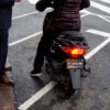 A man stands on the street talking to a woman on a motor-driven cycle.