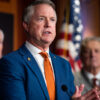 Sen Roger Marshall speaks at a podium in a blue suit and orange tie.