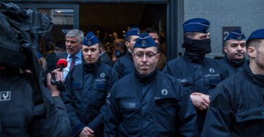 Several Brussels police officers in dark blue uniforms and caps block the entrance to a hotel