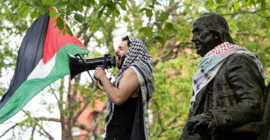 Male pro-Palestinian protester with Palestinian flag, headdress, and a megaphone alongside a bronze statue of Benjamin Franklin