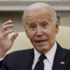 President Joe Biden in a suit with an American flag pin holds his hand near his head