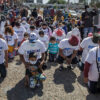 Migrants kneel wearing t-shirts reading "Biden please let us in" near the U.S.-Mexico border.