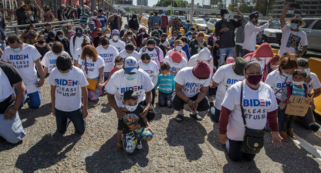 Migrants kneel wearing t-shirts reading "Biden please let us in" near the U.S.-Mexico border.