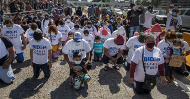 Migrants kneel wearing t-shirts reading 