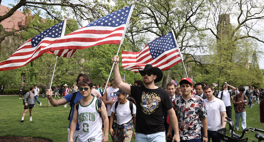University of Chicago counter-protesters raise American flags into the air, wearing t-shirts.