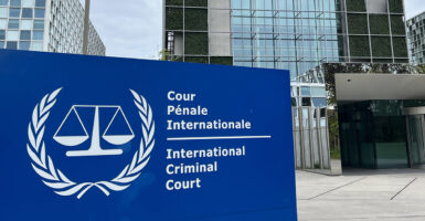 A blue sign with white lettering labeled international criminal court outside a glass and steel court building