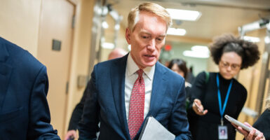 James Lankford in a blue suit looks down, holding paper and walking in a hallway.