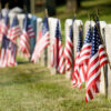 American flags seen flying in front of a row of tombstones.
