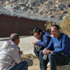 Chinese immigrants sit on the ground next to the U.S. border wall