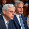 FBI Director Chris Wray sits behind Attorney General Merrick Garland as both wear suits
