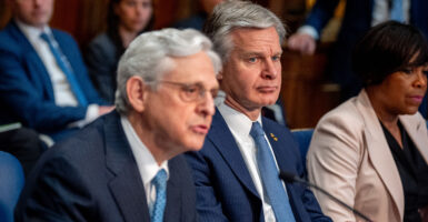 FBI Director Chris Wray sits behind Attorney General Merrick Garland as both wear suits