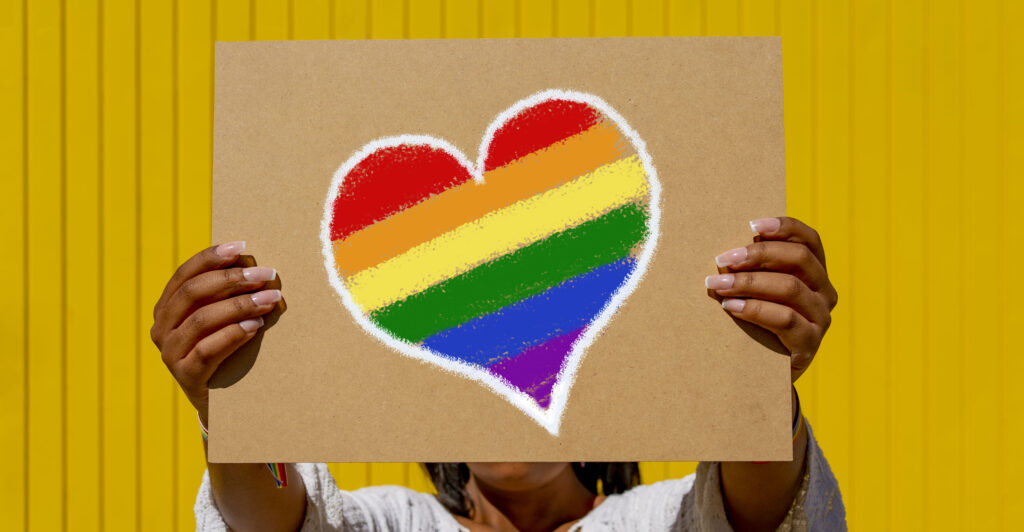 A woman holds a rainbow heart sign.