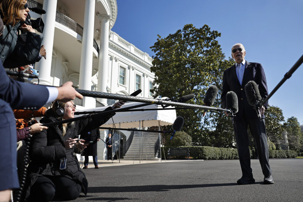 Joe Biden talks to reporters extending microphones to him in front of the White House.