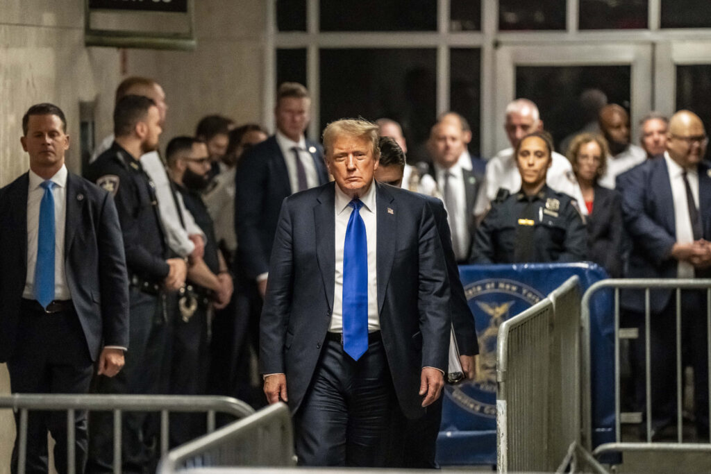 Donald Trump walks toward the camera wearing a blue tie and suit.