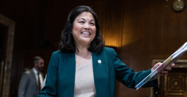 Acting Labor Secretary Julie Su smiles while holding out a binder and wearing a gray sport coat over a blouse