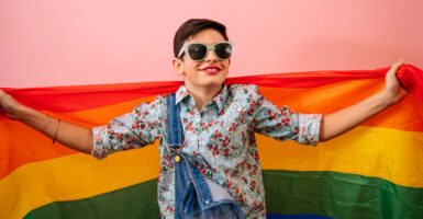 A young child smiling and holding an LGBTQ Pride flag.