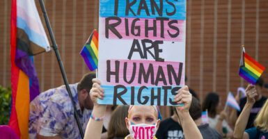 Woman holds sign reading "Trans Rights Are Human Rights" while wearing a face mask with the text "Vote."
