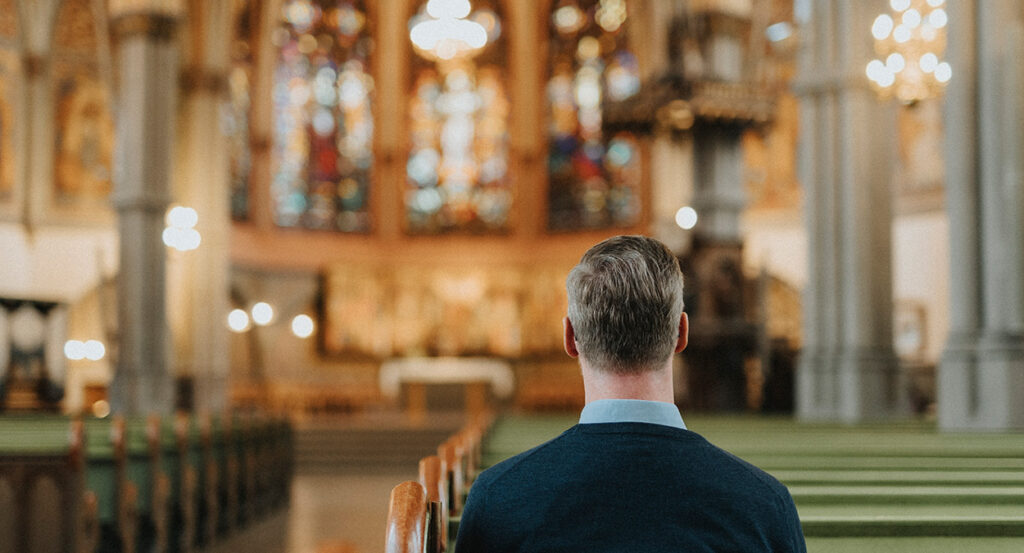 A man sits in a pew in a Catholic cathedral.