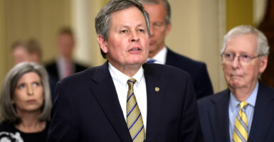 Sen. Steve Daines stands in front of several other senators in a suit and tie