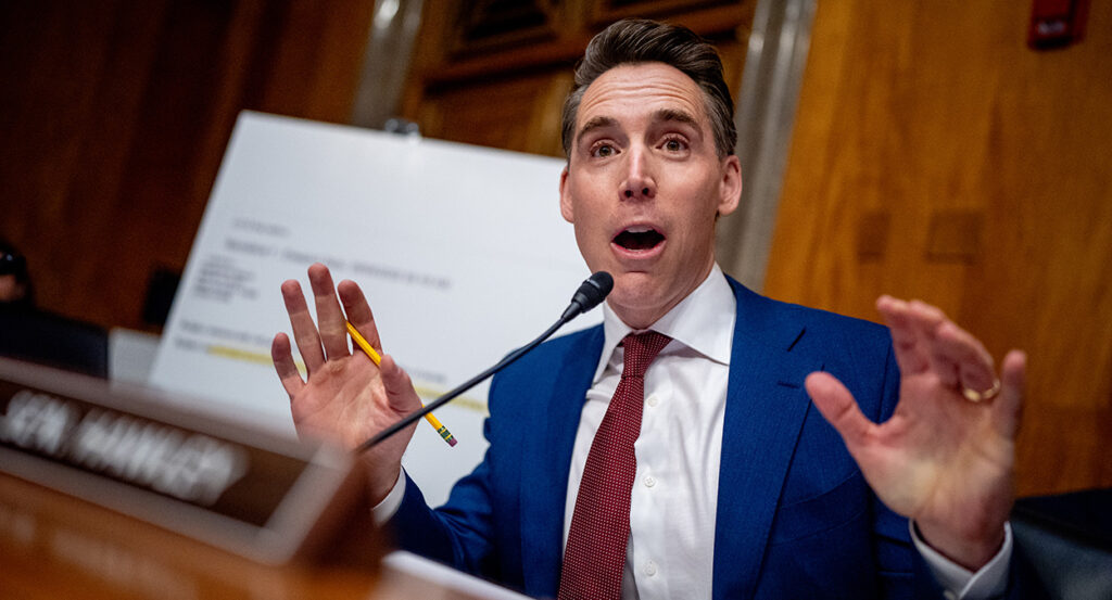 Sen. Josh Hawley holds up his hands and speaks into a microphone at a Senate hearing.