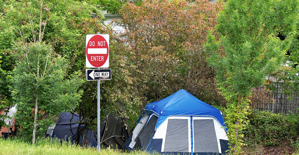 A tent in the forest behind a "Do Not Enter" road sign.