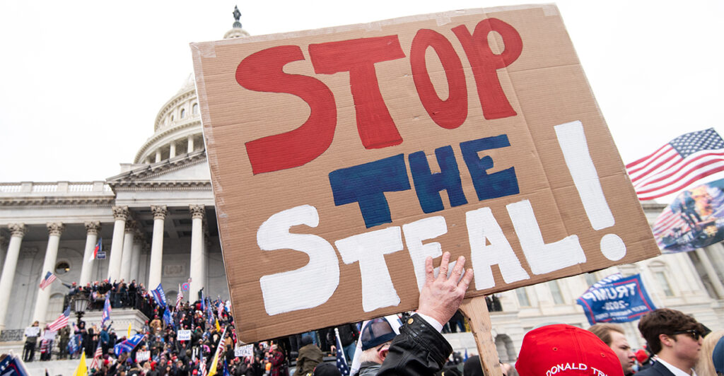 A man holds a hand-painted "stop the steal" sign with a large crowd of protesters standing in front of the U.S. Capitol on January 6, 2021