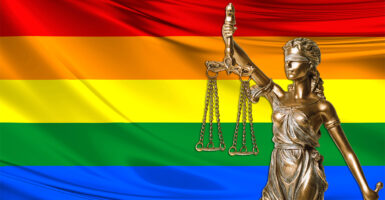 Statue of Lady Justice with an LGBTQ flag in the background