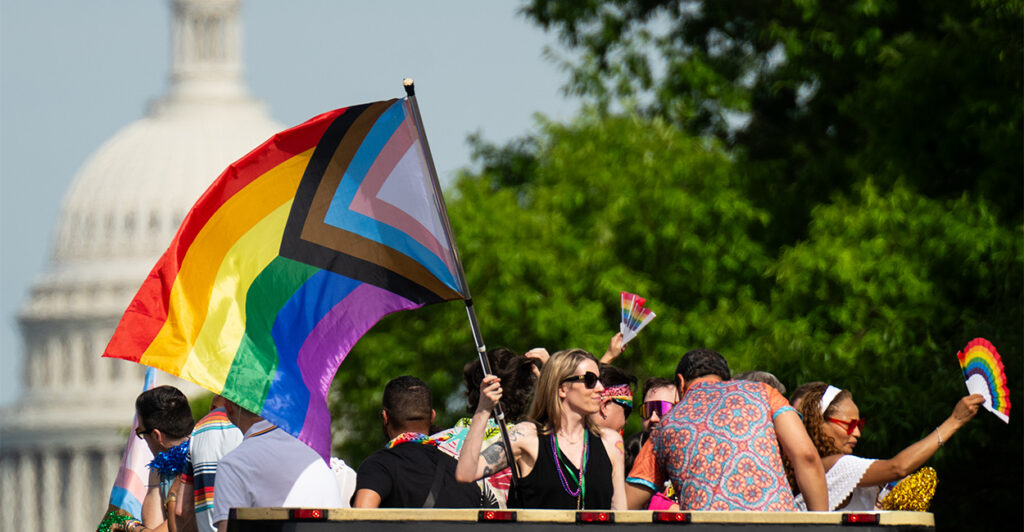 Parade-goers in Washington, DC, Wave the LGBTQ pride flag with the U.S. Capitol in the background