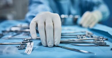 Surgeon picking up surgical tool from tray. Surgeon is preparing for surgery in operating room.