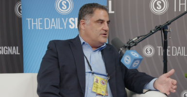 Cenk Uygur speaks at The Daily Signal booth wearing a suit without a tie