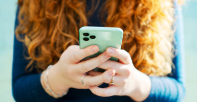 A young woman holding a cell phone with both hands.