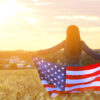 Silhouette of woman with the American flag in a wheat field against the sunset.