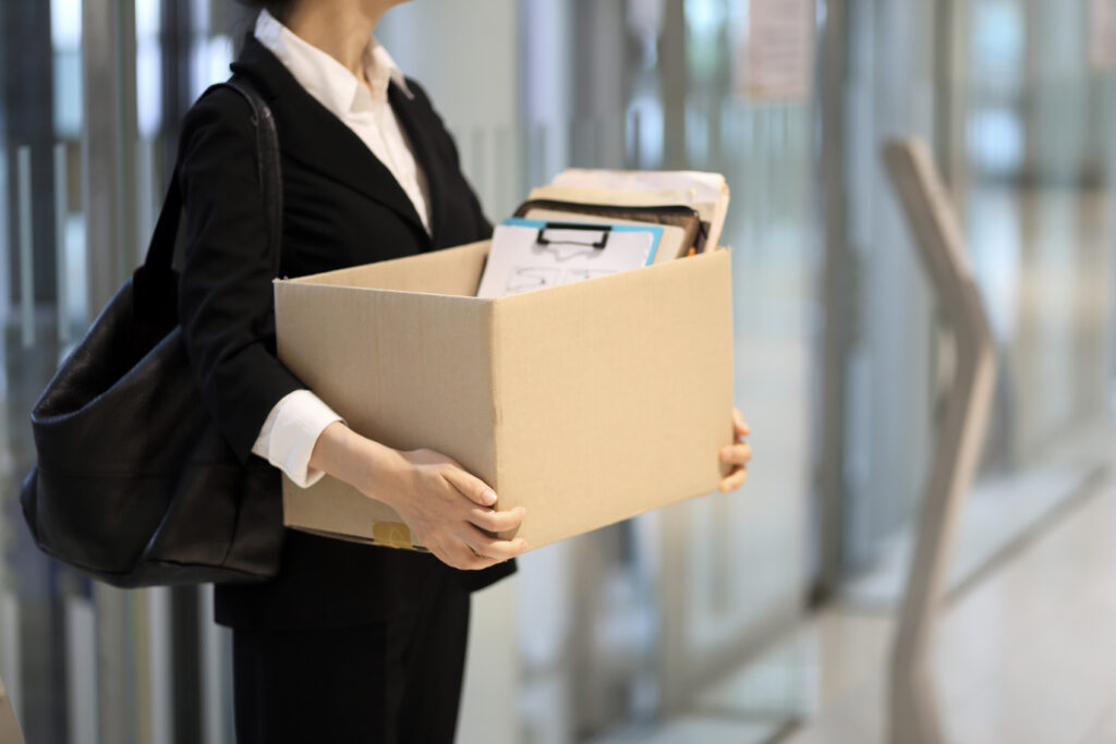 A woman wearing a pantsuit holds a box of her belongings.