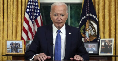 President Joe Biden in a black suit with a blue tie in the Oval Office