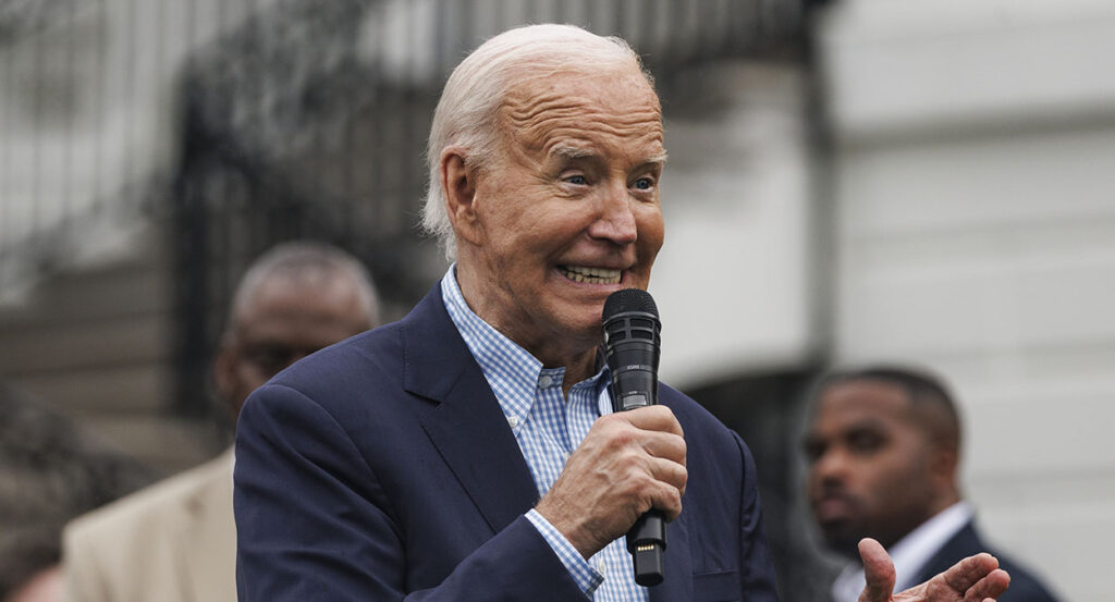Joe Biden in a blue suit grits his teeth and holds a microphone