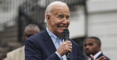 Joe Biden in a blue suit grits his teeth and holds a microphone