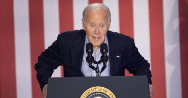 Joe Biden in a blue suit leans forward on a podium with the presidential seal