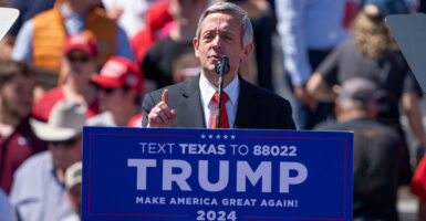 Robert Jeffress in a suit stands behind a podium reading "TRUMP Make America Great Again!"