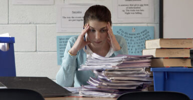 Teacher holds her head and looks at papers