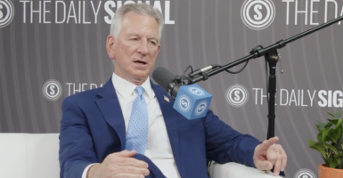Tommy Tuberville in a blue suit sits in front of The Daily Signal