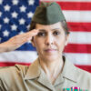 A female U.S. soldier saluting in front of an American flag.