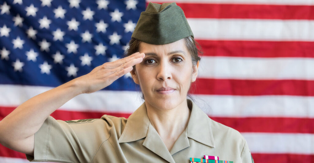 A female U.S. soldier saluting in front of an American flag.
