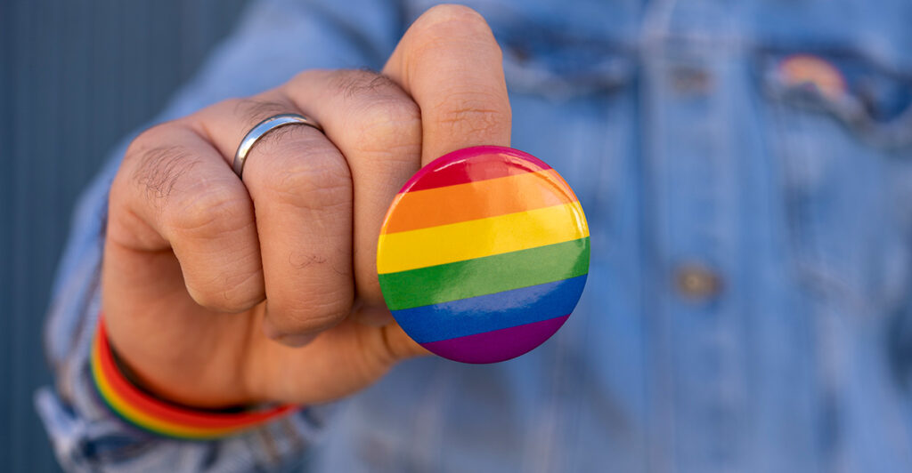 A man holds a rainbow pin.